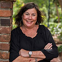 Wanda is pictured from the shoulders up wearing a black shirt. She has tan skin, dark brown hair, and is smiling. 