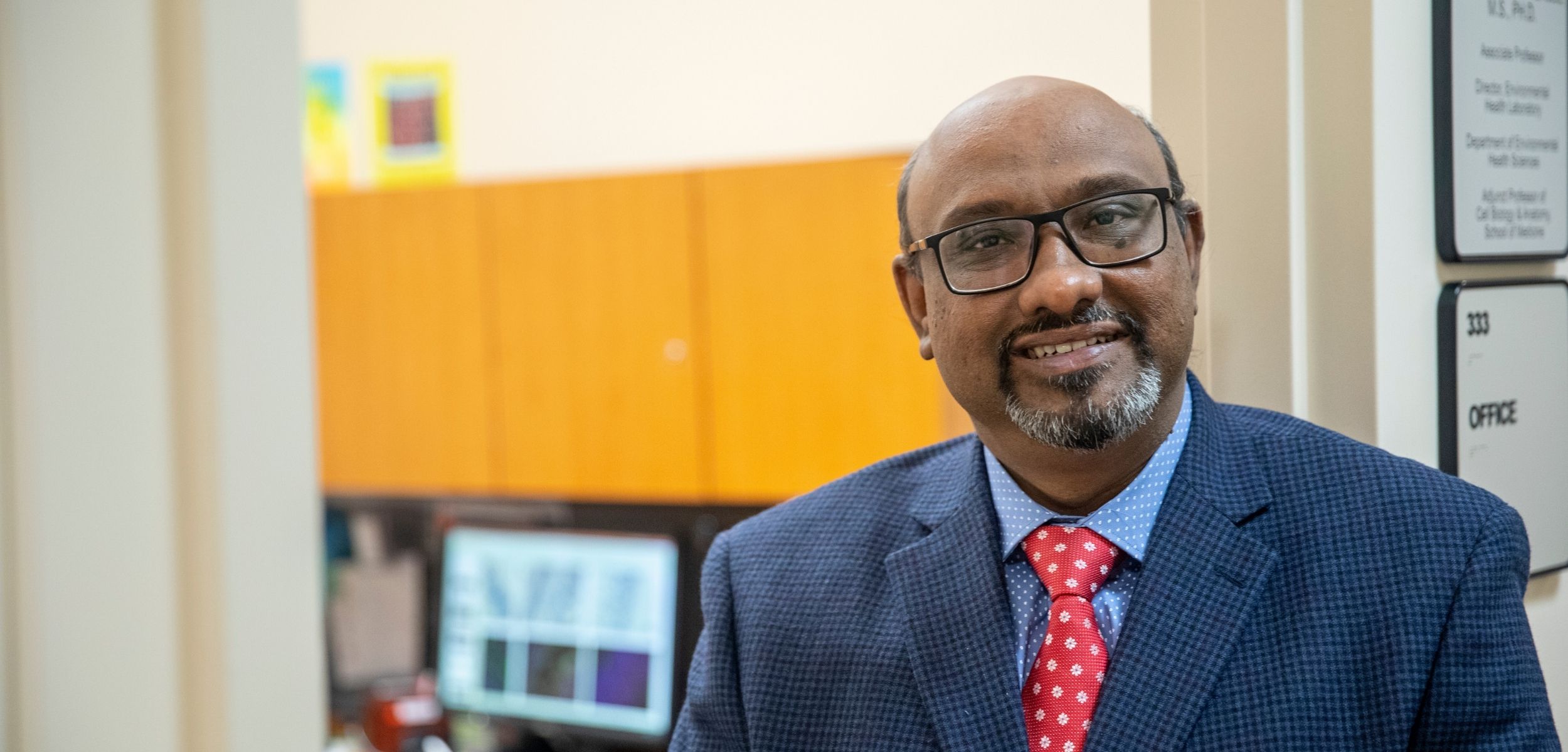 Male faculty member smiling in front of office. 