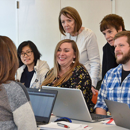 A group of people standing and seated around a smiling woman working on a laptop.