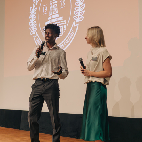 two honors ambassadors smiling and holding microphones
