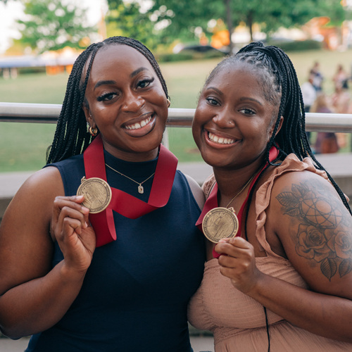 Two students smiling and holding up their gold Honors medallions