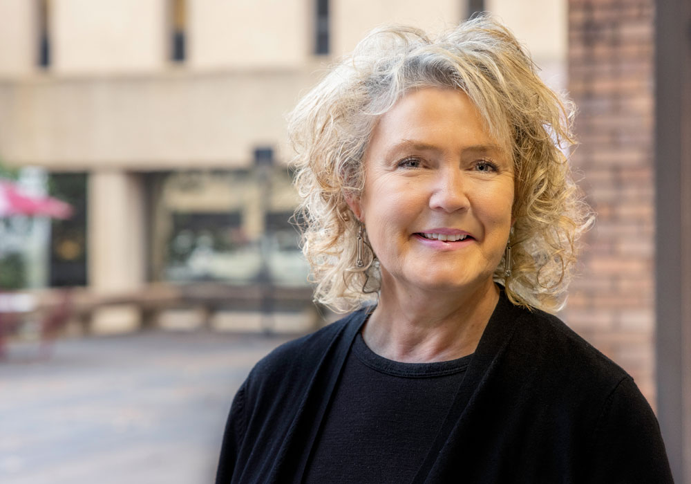 An environmental portrait of Lorie Donelle standing in front of the College of Nursing.